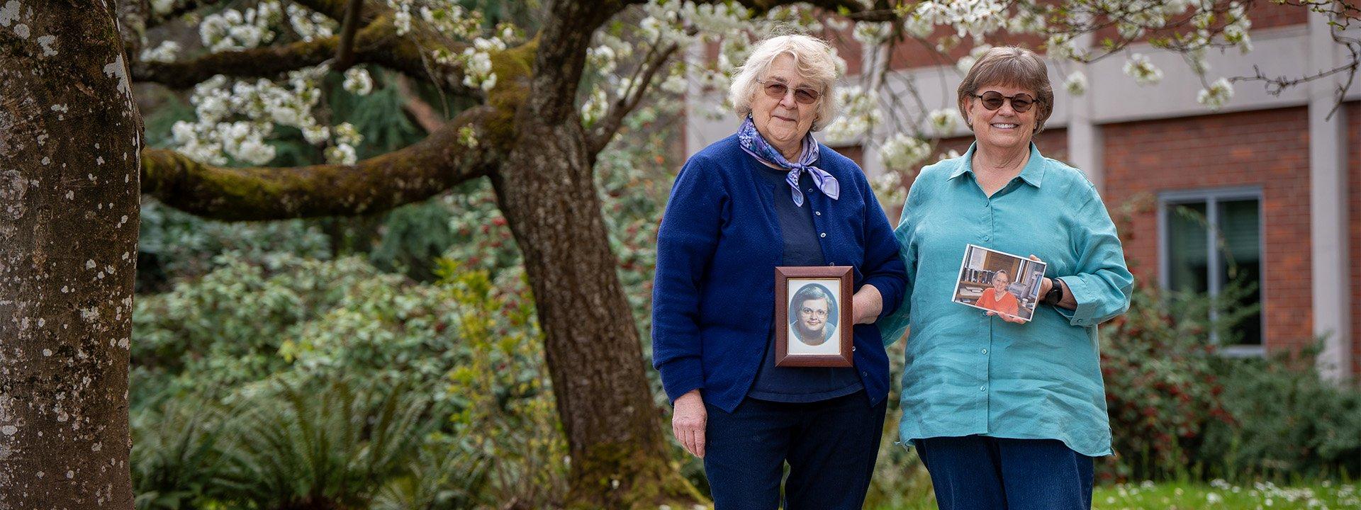 Anne Laskaya and Linda Long holding framed pictures of Suzie Gerhardt and Peggy Pascoe