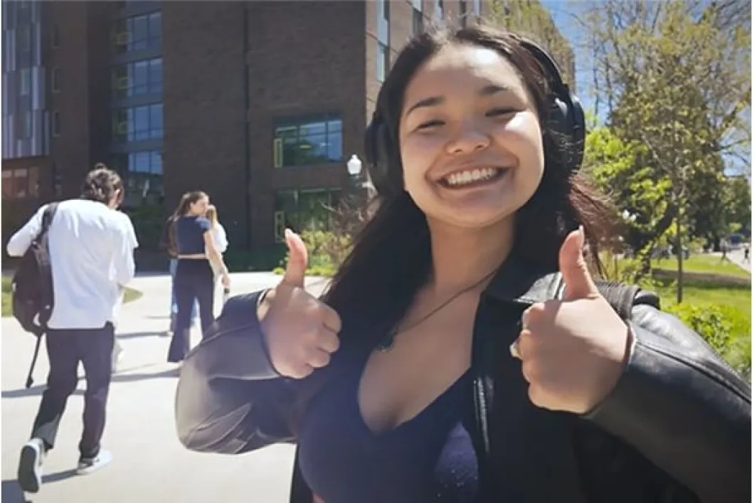 Catalina a student poses smiling for the camera giving a double thumbs up