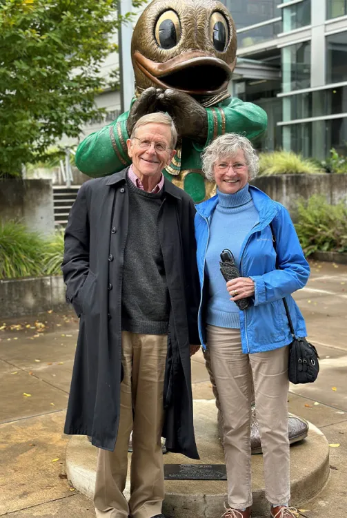 Roger Chickering and Alison Baker stand in front of a statue of the Oregon Duck