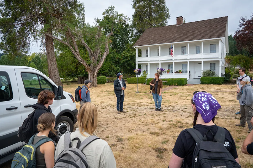 Students standing in a circle outside of a 2-story white house