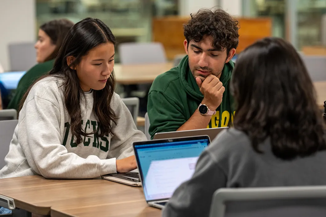 Students in UO gear working on laptops at Knight Library.