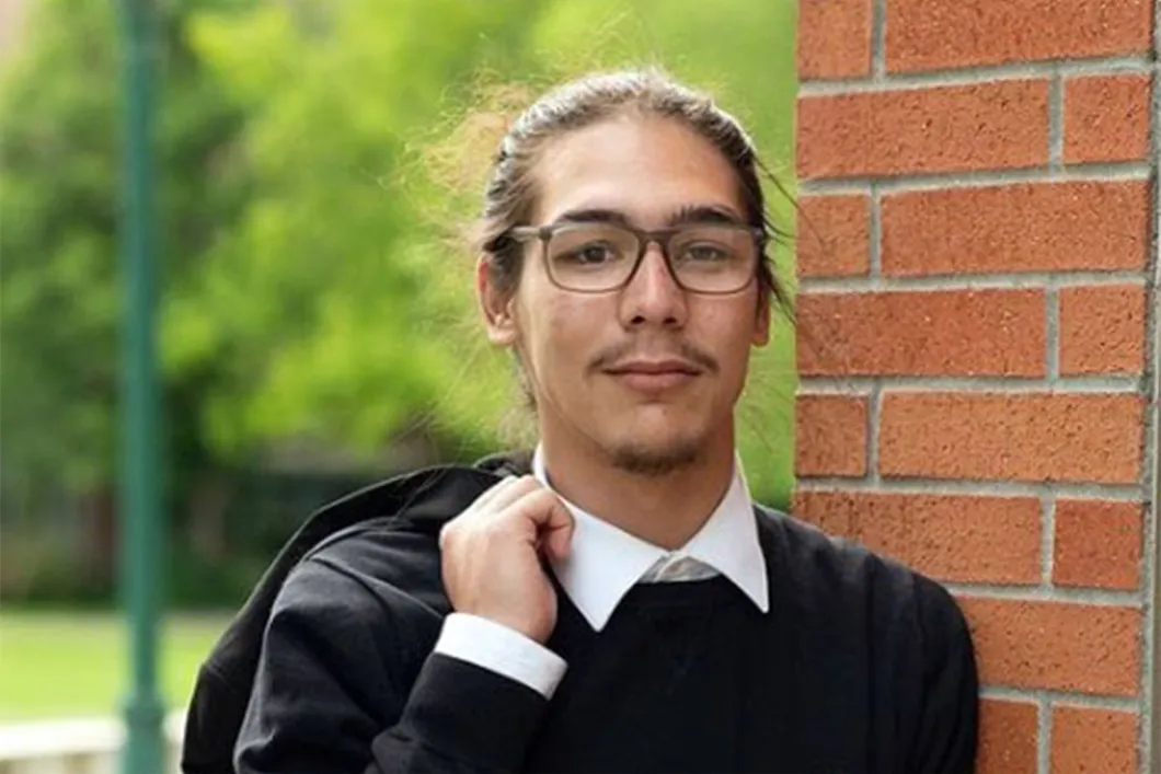 Young man in glasses standing by a brick wall