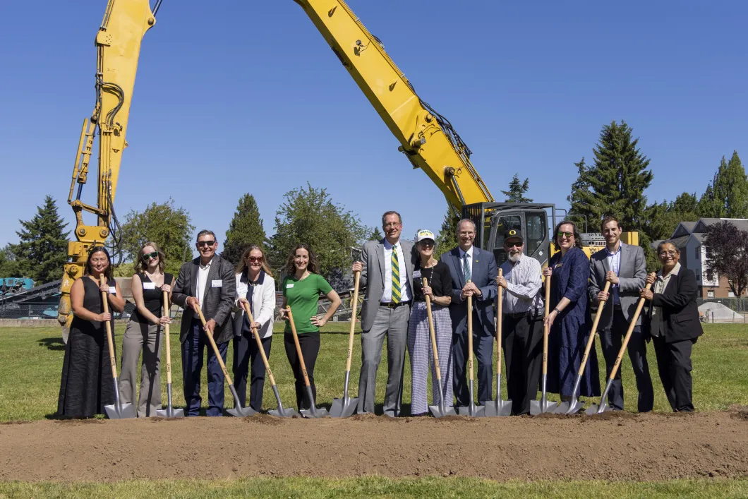 People stand with shovels in front of a crane. 