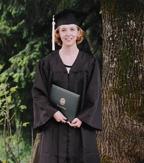 woman wearing graduation cap and gown holding a diploma cover