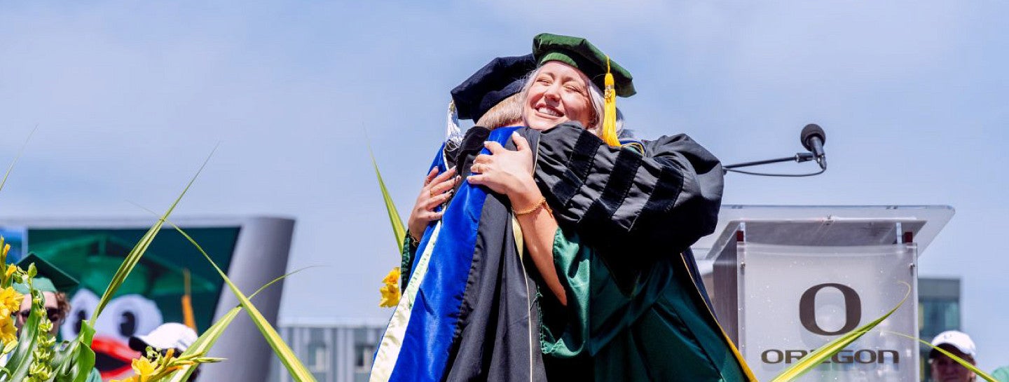 Doctoral student in commencement regalia hugging a faculty member.