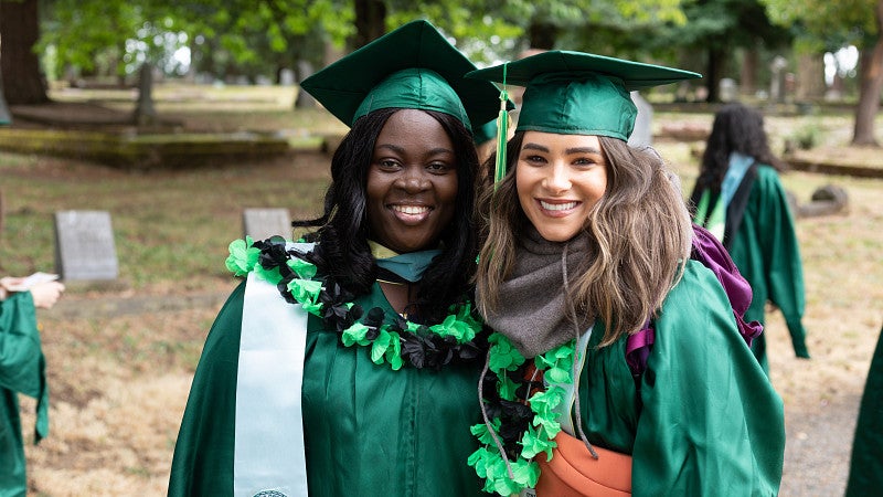 Two master's students in graduation regalia smiling.