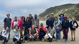 15 graduate students and 4 staff members from the Outdoor Program smiling together on the Oregon Coast