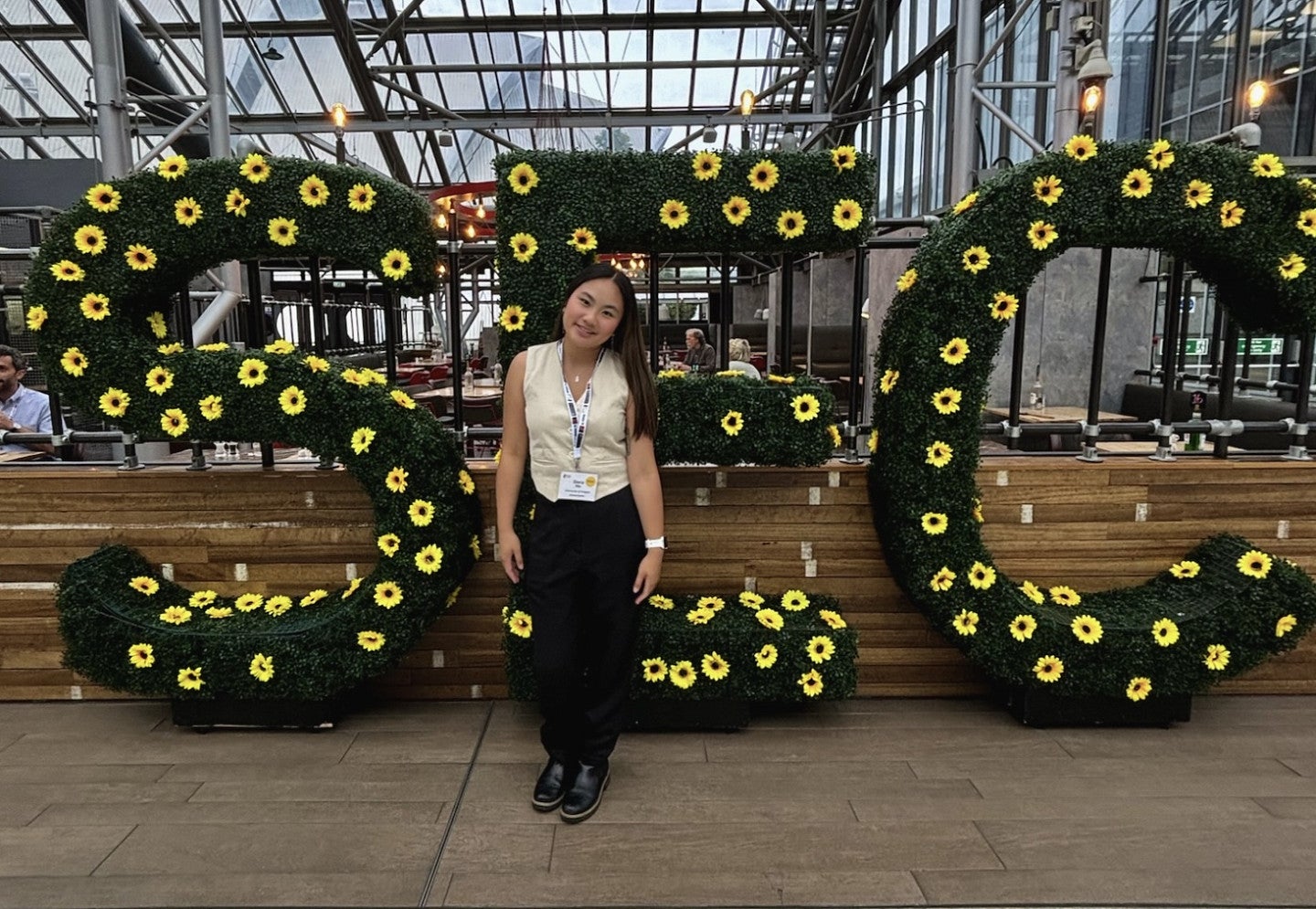 Woman standing in front of shrubbery with the letters "SEC" in yellow