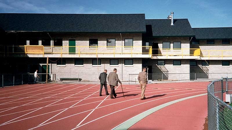Former track coach Bill Bowerman and two other men walking on the Hayward Field track, away from camera towards the Bowerman Building 