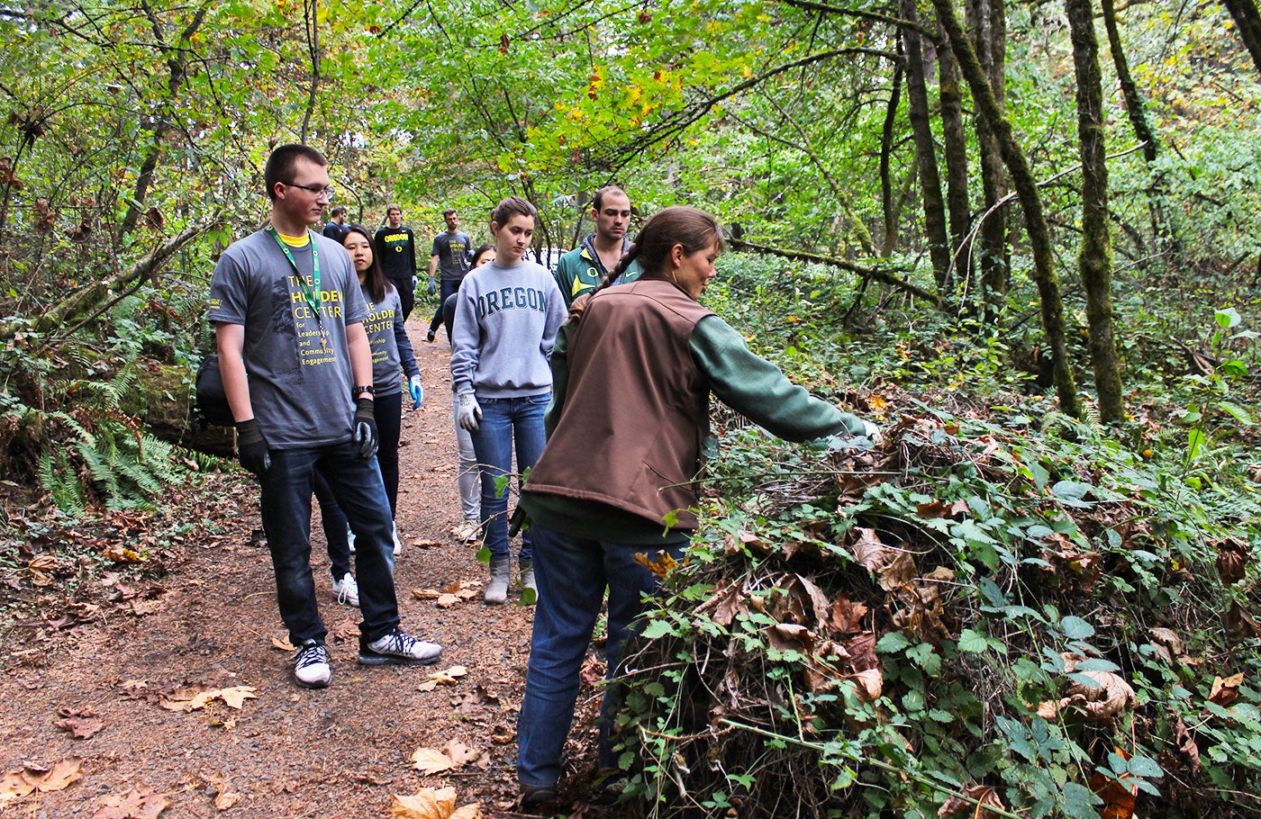 Students clearing leaves and invasive plants from walking path.