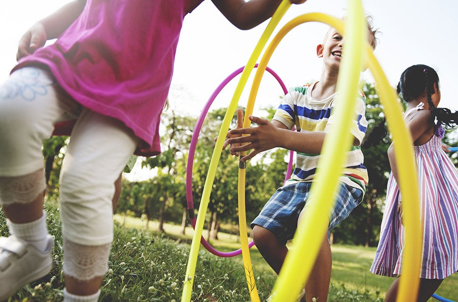 Children on grass playing with hula hoops.