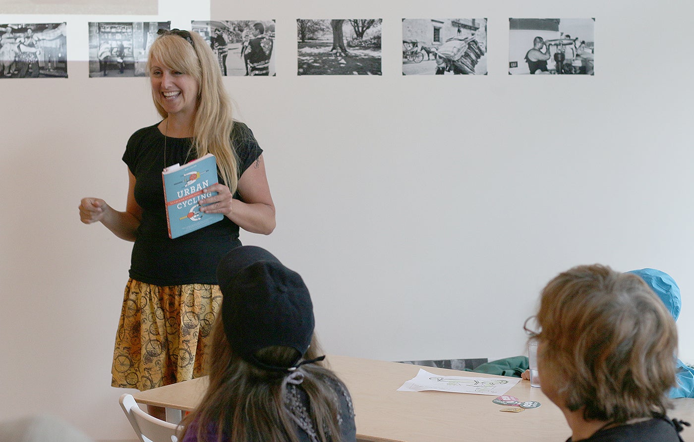 Woman with blond hair speaking to young students.