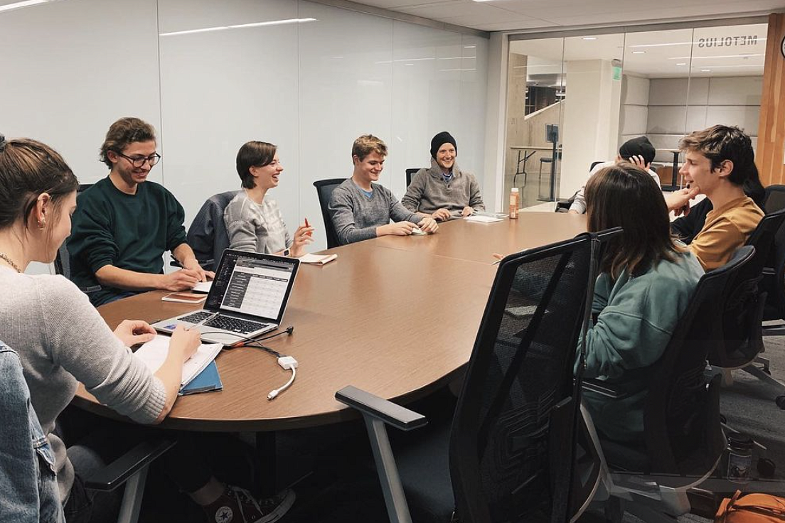 Students from the Unbound Journal group sitting at a round table together, smiling and working. 