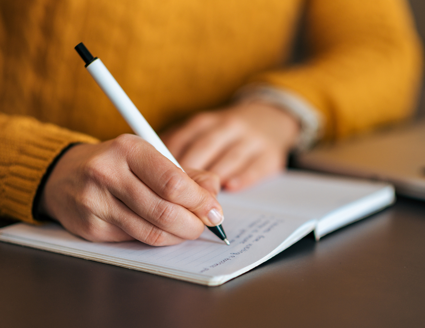Person in yellow sweater writing in notebook