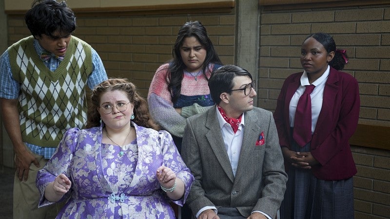 group of five people dressed in costumes like elementary school students and principals all looking at each other with upset expressions 