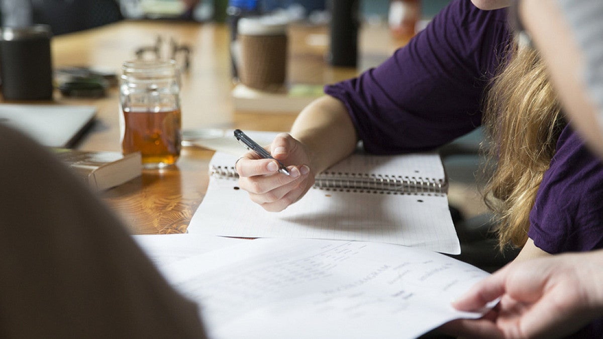 Student writing in a notebook at a desk.