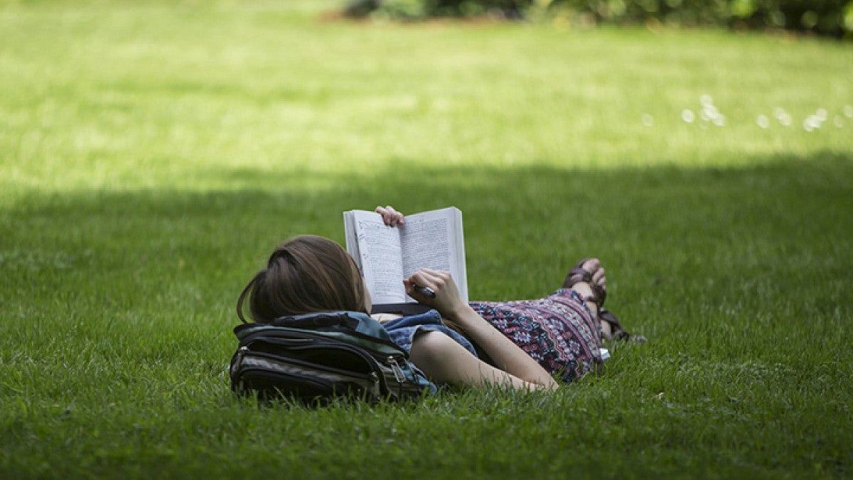 Student lying on the grass outdoors, reading a book.