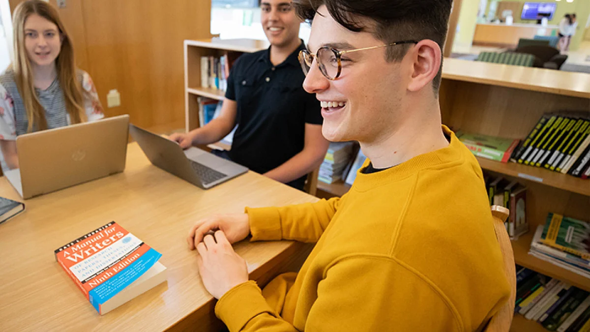 Three students sitting around a desk, smiling and working together.