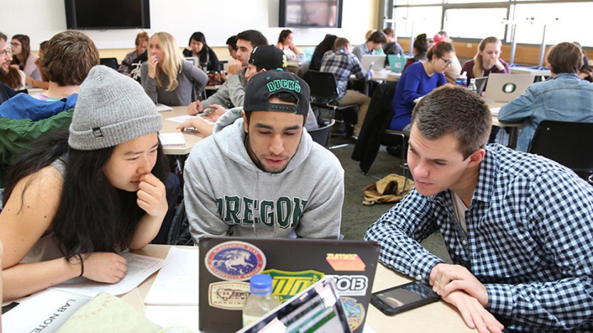 Three students focused on the same work on a computer.