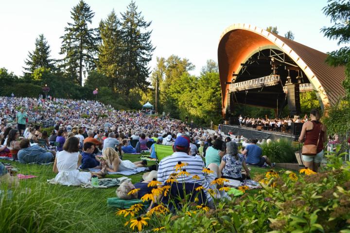 People sit on blankets in front of a Eugene amphitheater on a clear sunny day.