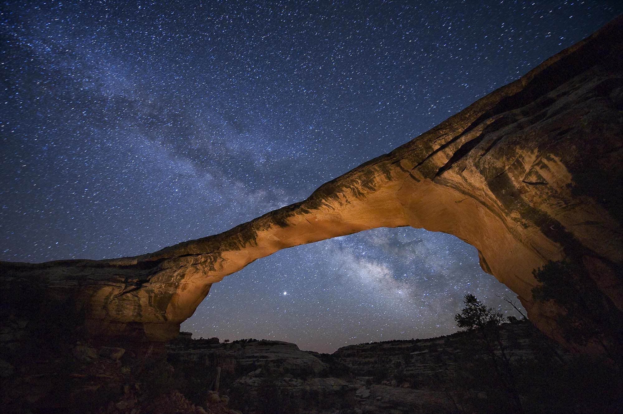 Natural stone bridge lit from below with a brilliant starfield above
