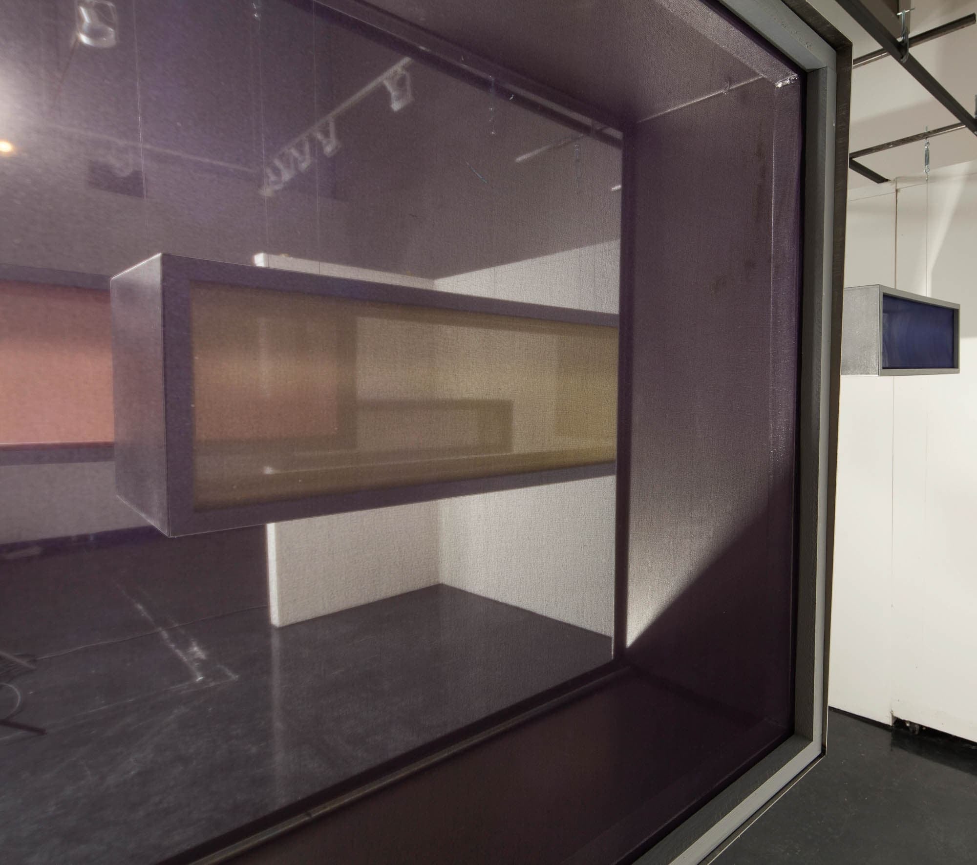 Various boxes hanging from the ceiling with a close up view of one. The sides are transparent and they hang in a gallery.