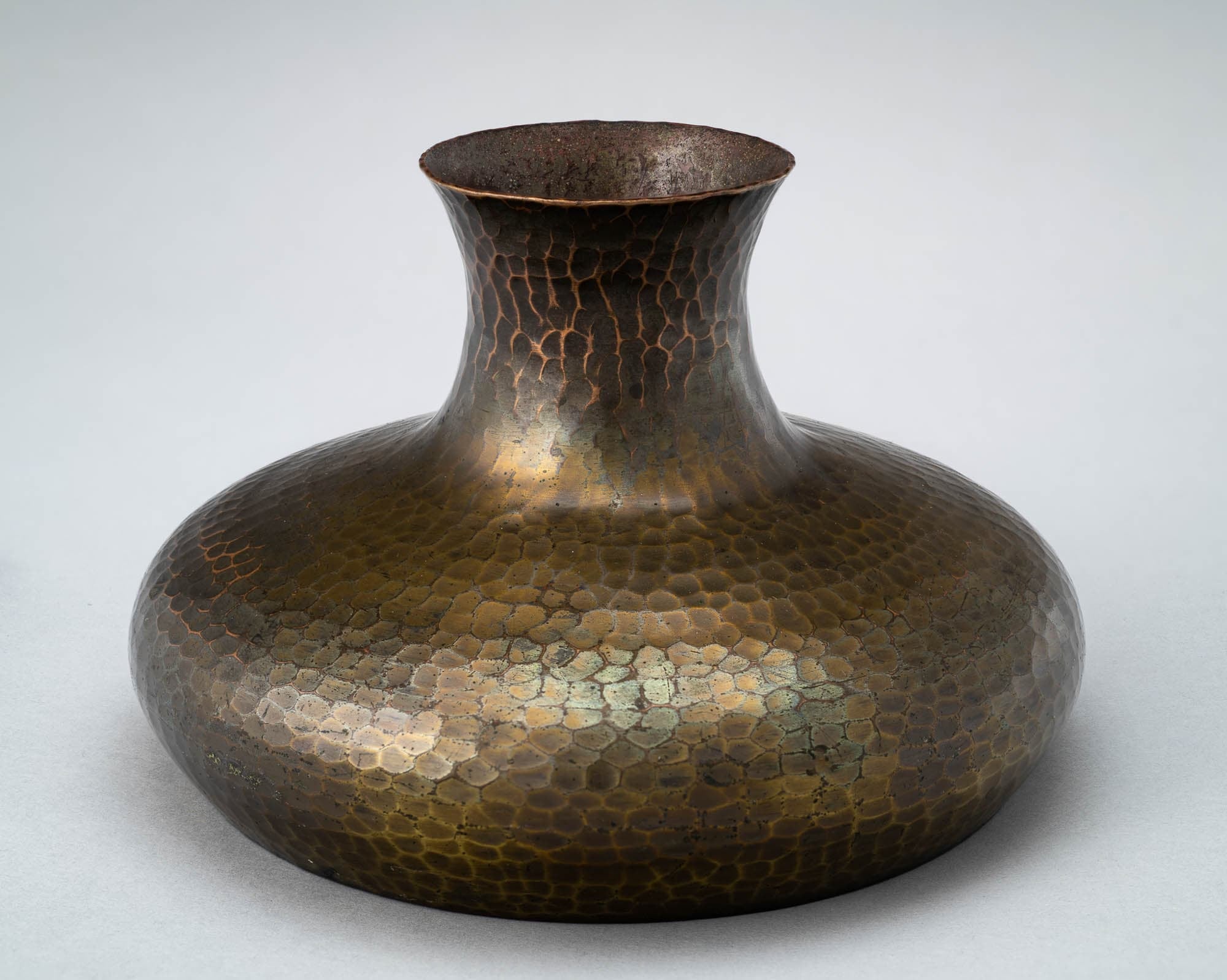 A hammered copper vase with a wide, rounded base and a narrow neck. The patina and texture of the metal give it an antique and artisanal look.