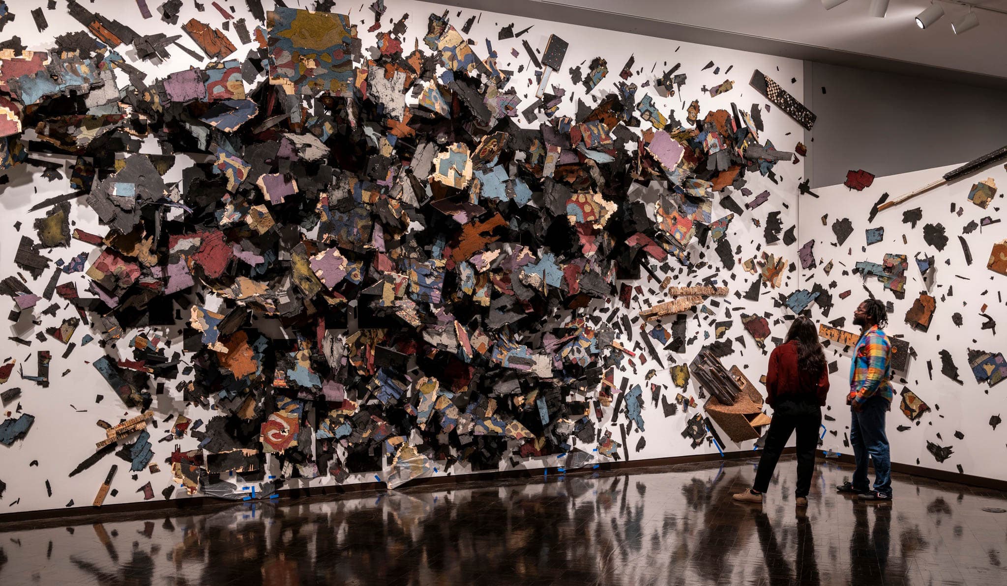 Two people stand in front of a 3-dimensional art installation stretching across 2 walls