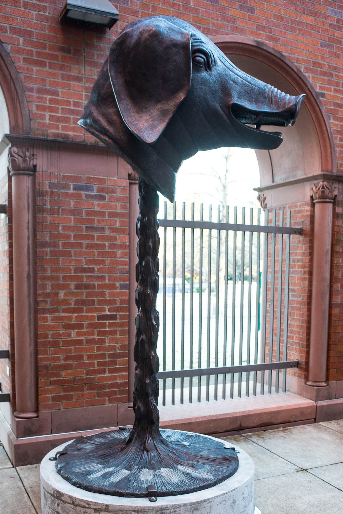 A bronze sculpture of a pig's head on a tall plinth, part of a courtyard installation set against a brick building.