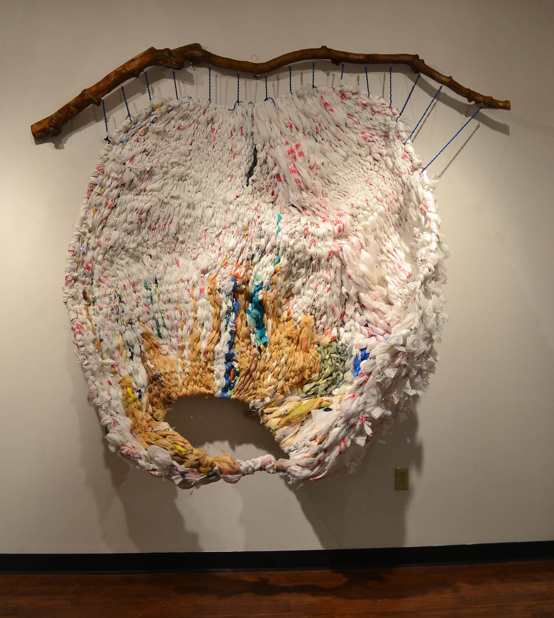 A sculptural installation made of repurposed plastic bags and fabric, creating a large, textured nest-like structure.