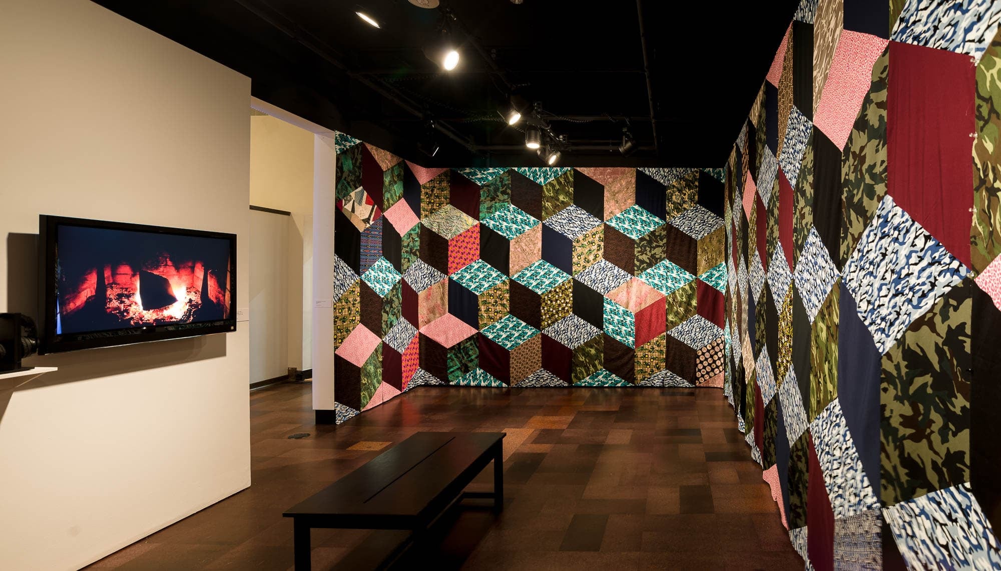 Installation of a quilt-like artwork with a television displaying a burning fireplace.