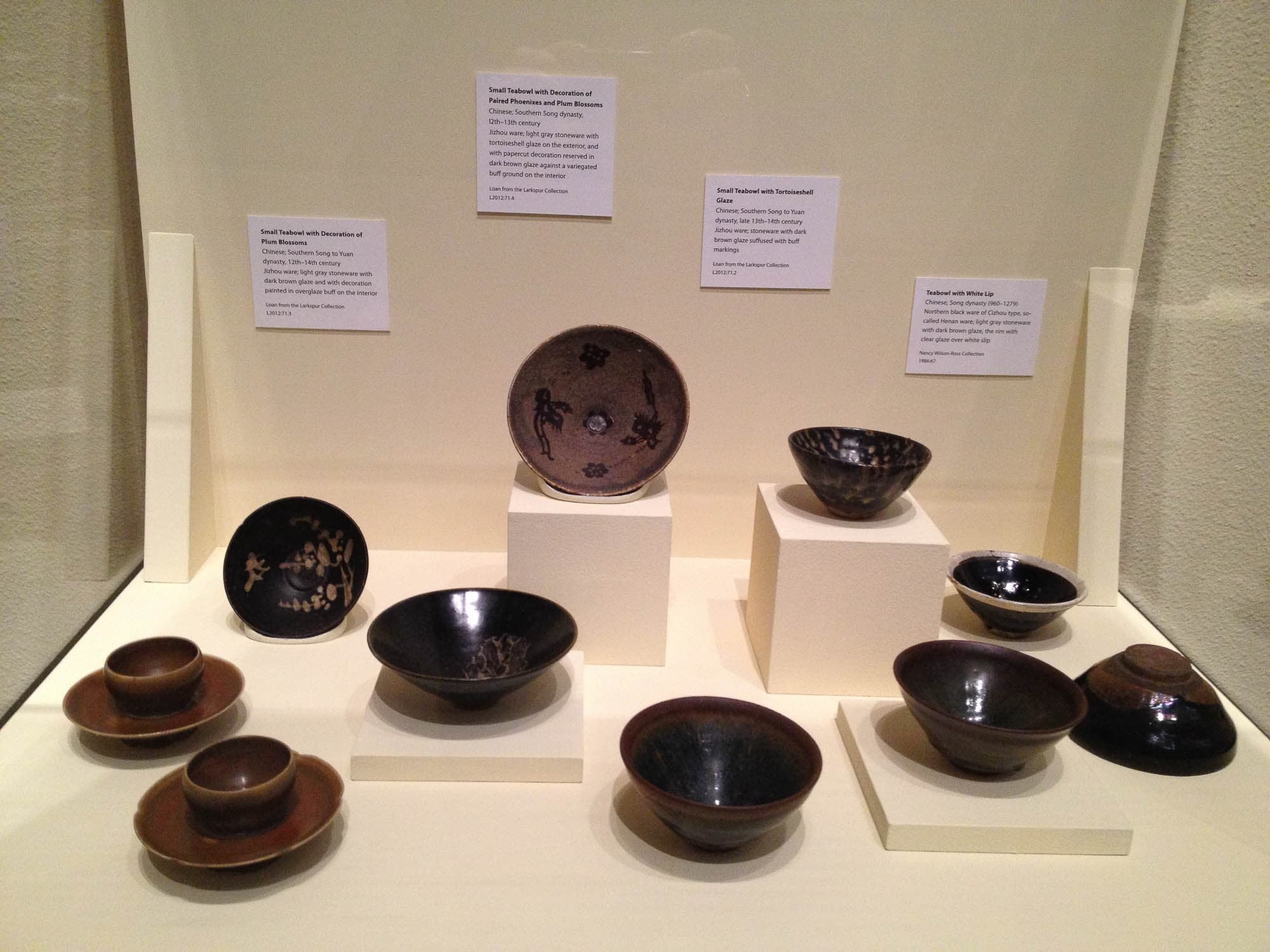 A display of various ceramic bowls and cups, labeled with descriptions, in a museum setting.