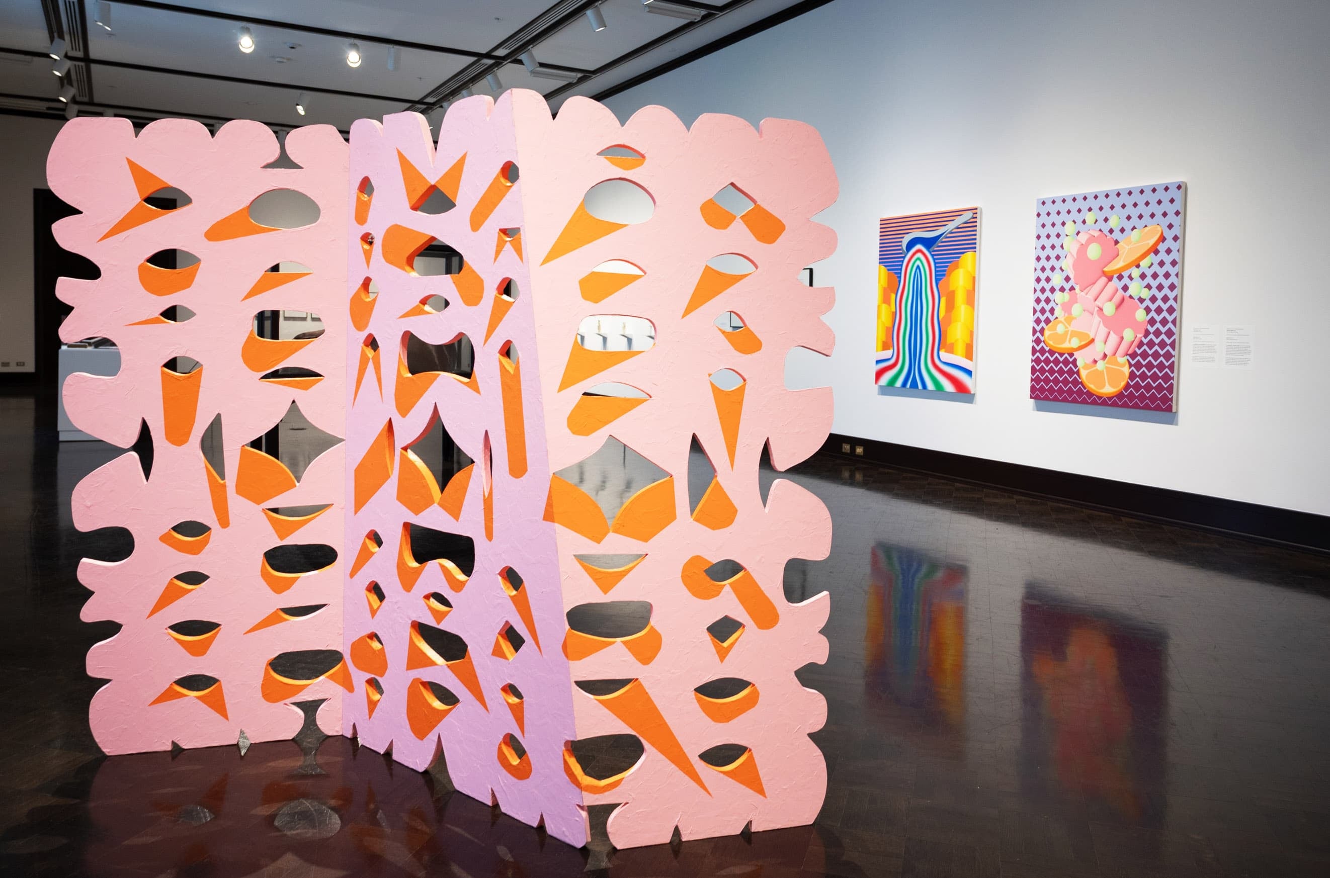 Gallery view with stylized screen like artwork in foreground and two colorful paintings in the background
