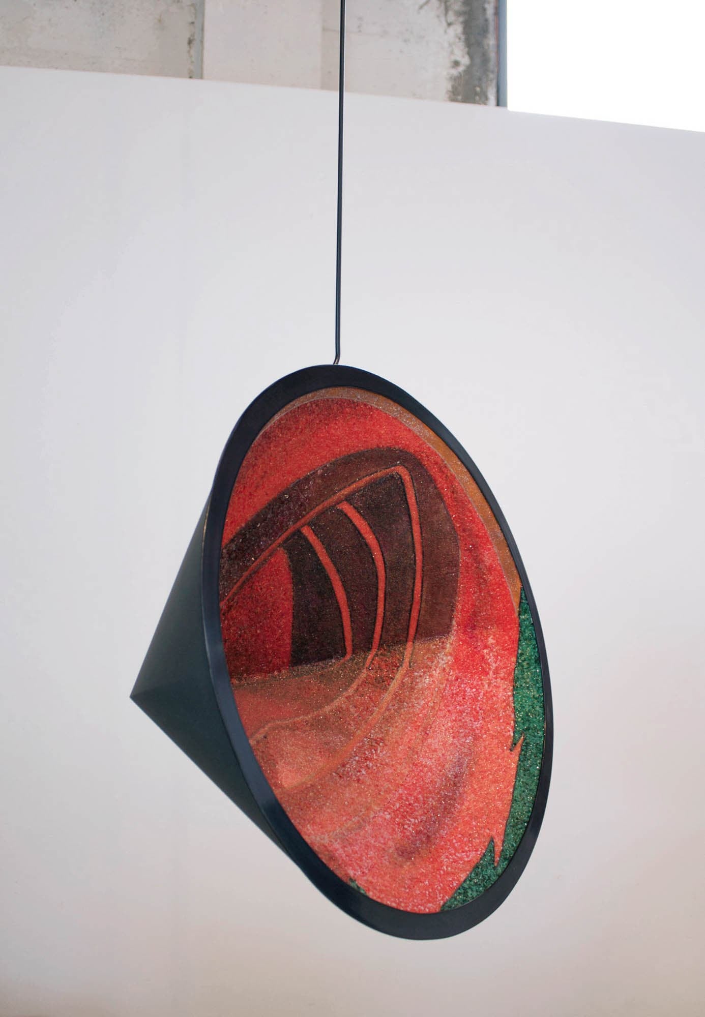 A hanging circular sculpture with a red, orange, and green abstract design inside, resembling an open mouth.
