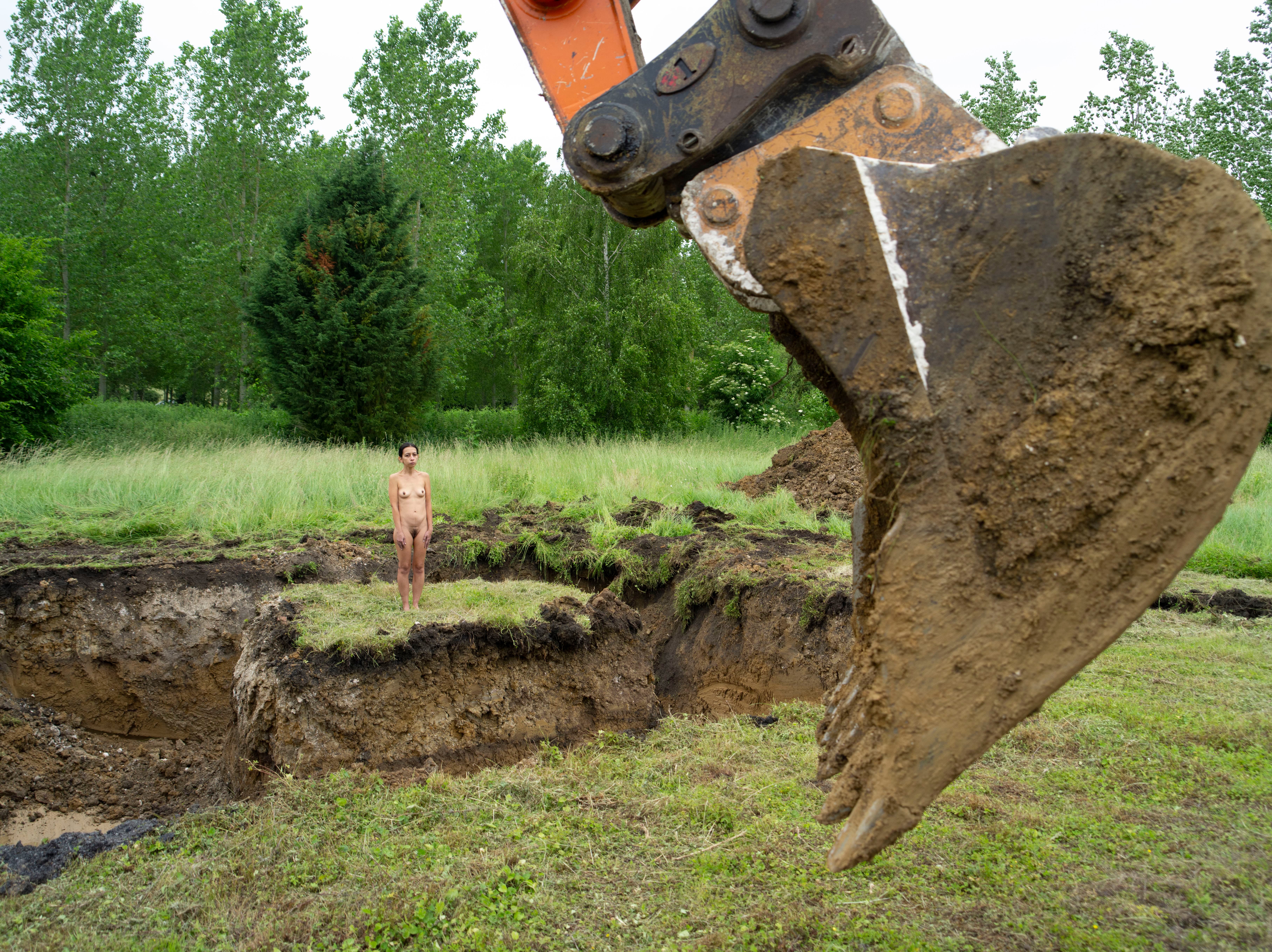 A small woman stands on a patch of land while a bulldozer digs up dirt around her