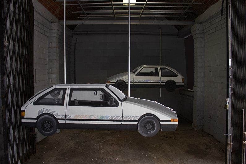White hatchback car levitating in a room with a concrete floor and gray bricks. A smaller inverse image of the car is in the background.