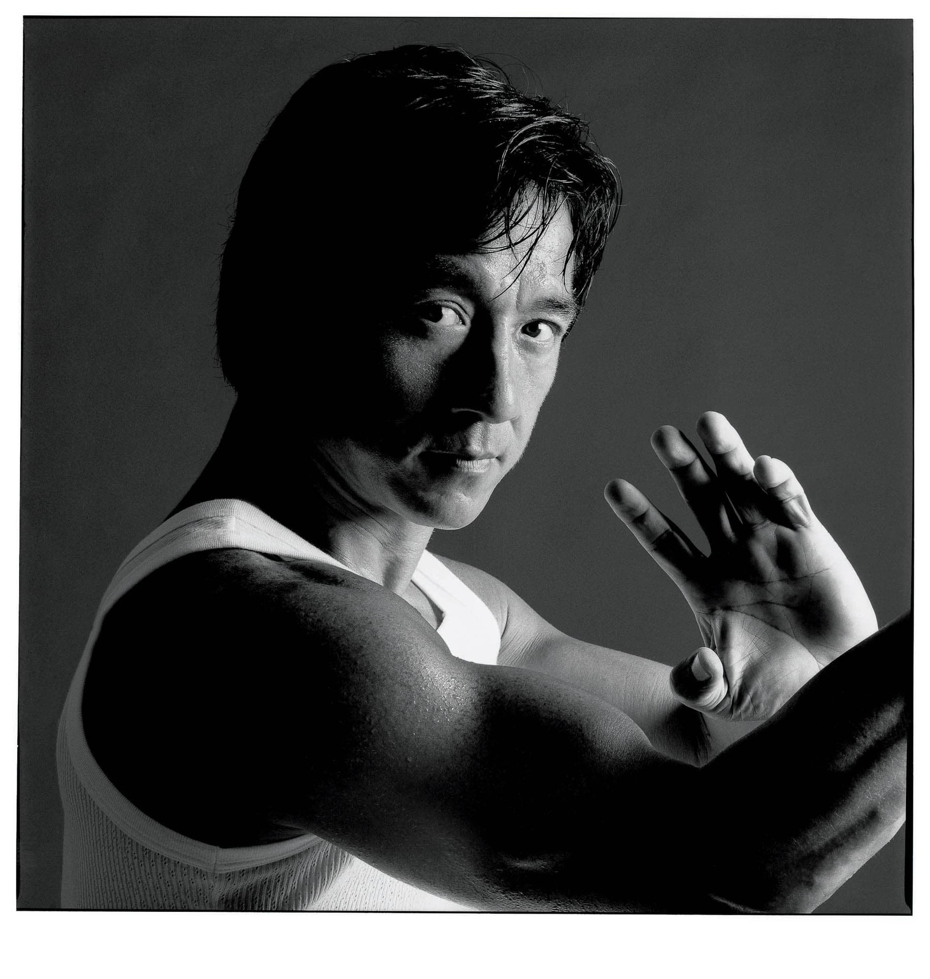 Black and white photograph of Jackie Chan’s face and upper body in martial arts pose