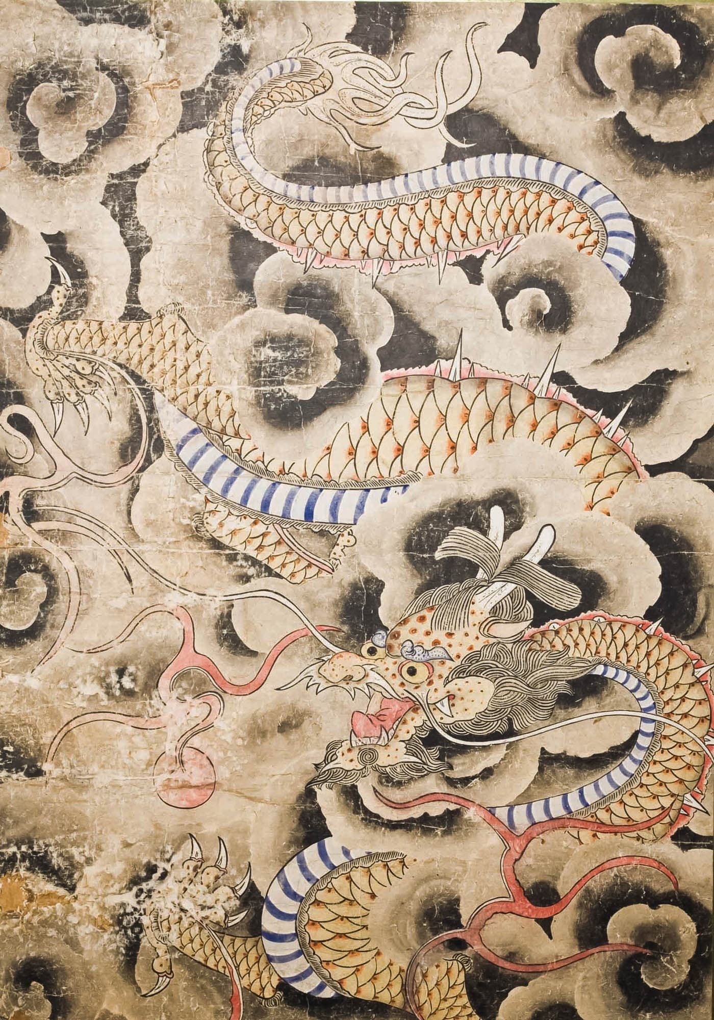 East Asian dragon snaking through black and light gray swirling clouds. The head is at the center bottom of the artwork with the tail at the top. The underside is striped blue and white, and the rest of the scales have red at the base.
