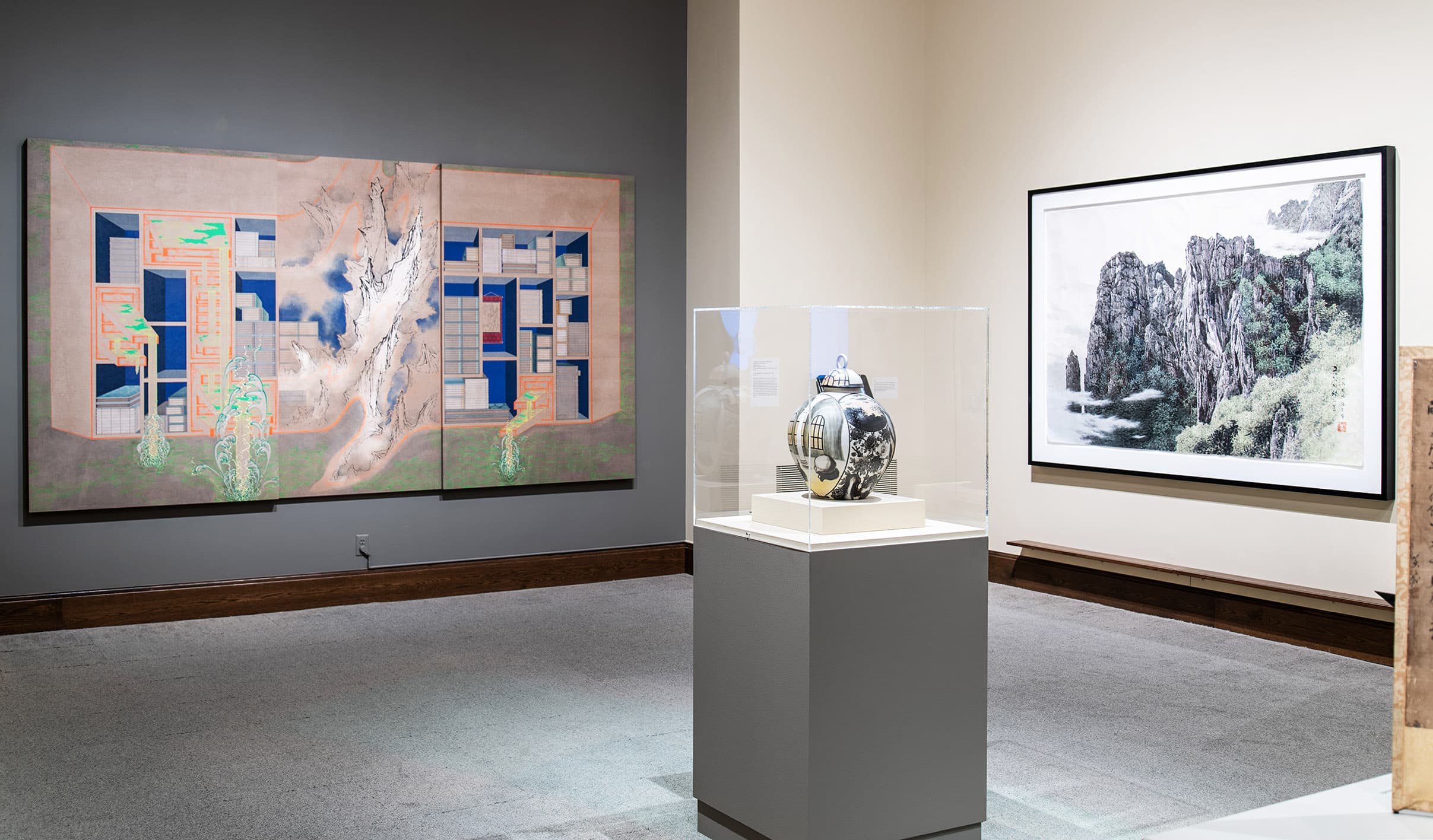 Gallery view of art exhibition with two paintings in an Asian style and a ceramic pot under a vitrine.