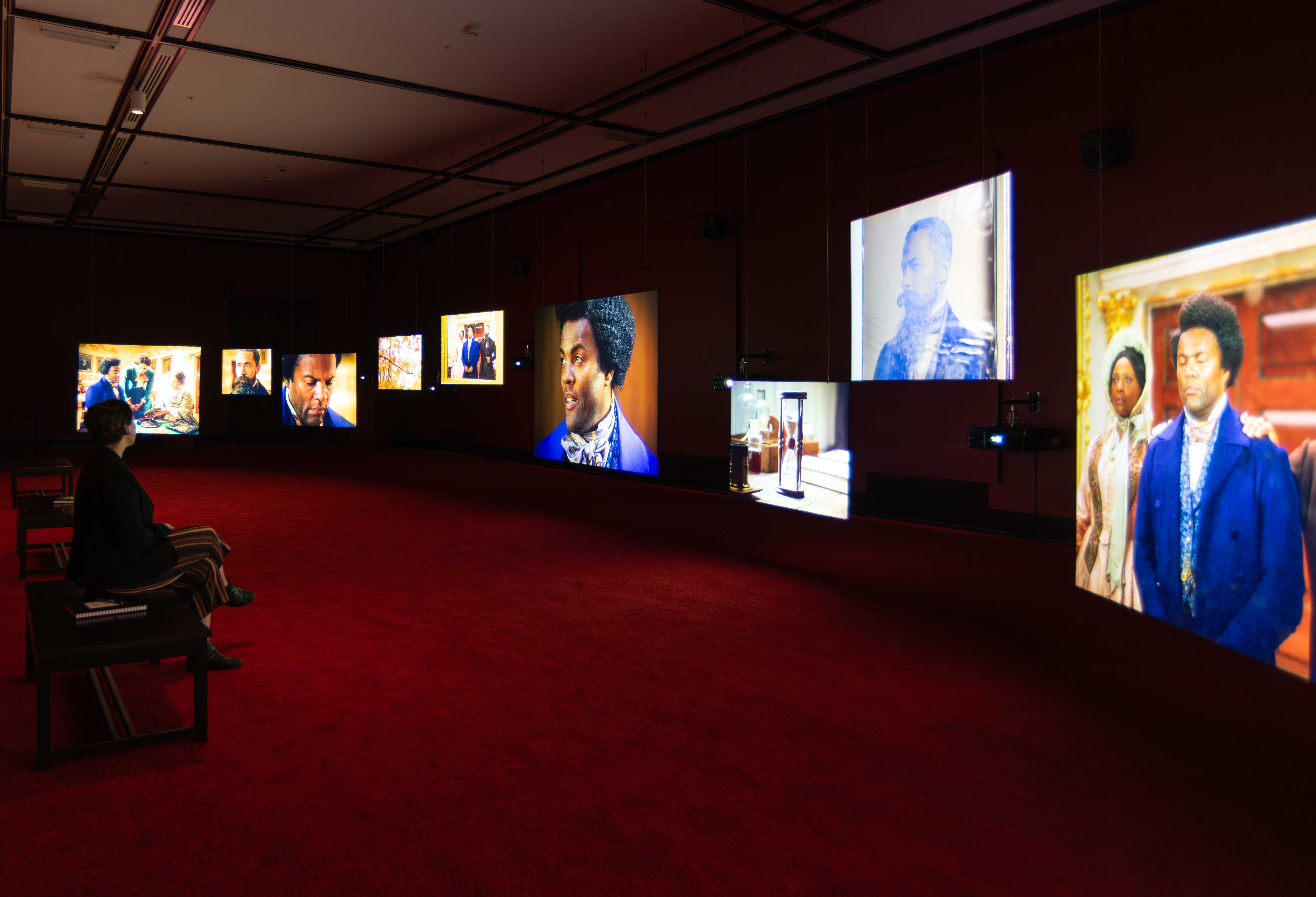 A woman sits in a darkened room lit only by the ten video screens showing images from Frederick Douglass' life.