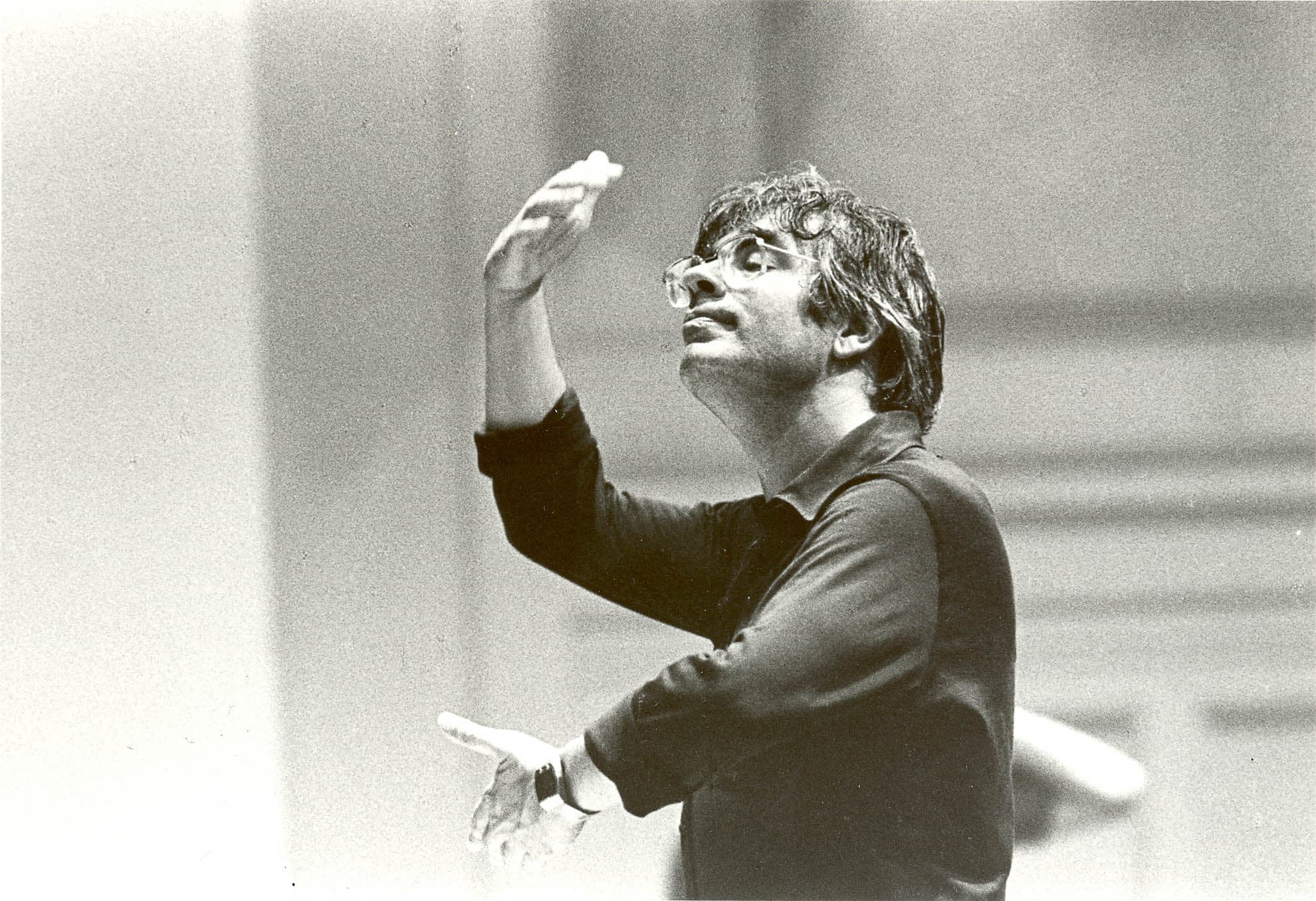 Black and white photography of a person with short dark hair wearing glasses and a dark shirt with hands held as though waltzing with an invisible person