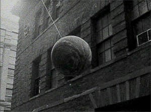 Black and white photo of a wrecking ball swinging alongside an old brick building