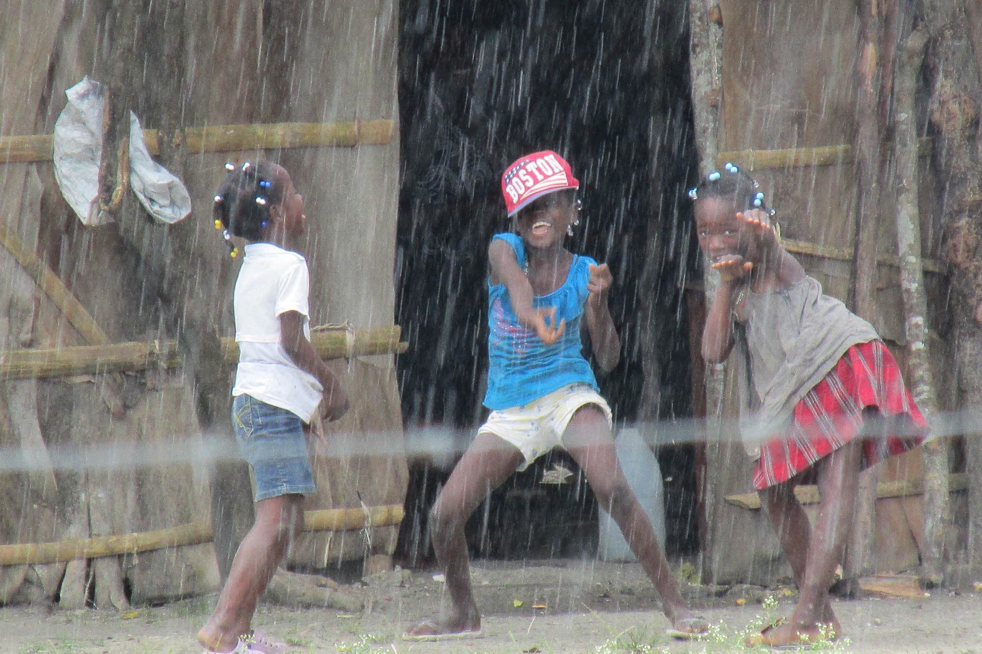 Photograph of 3 dark-skinned children dancing in the rain