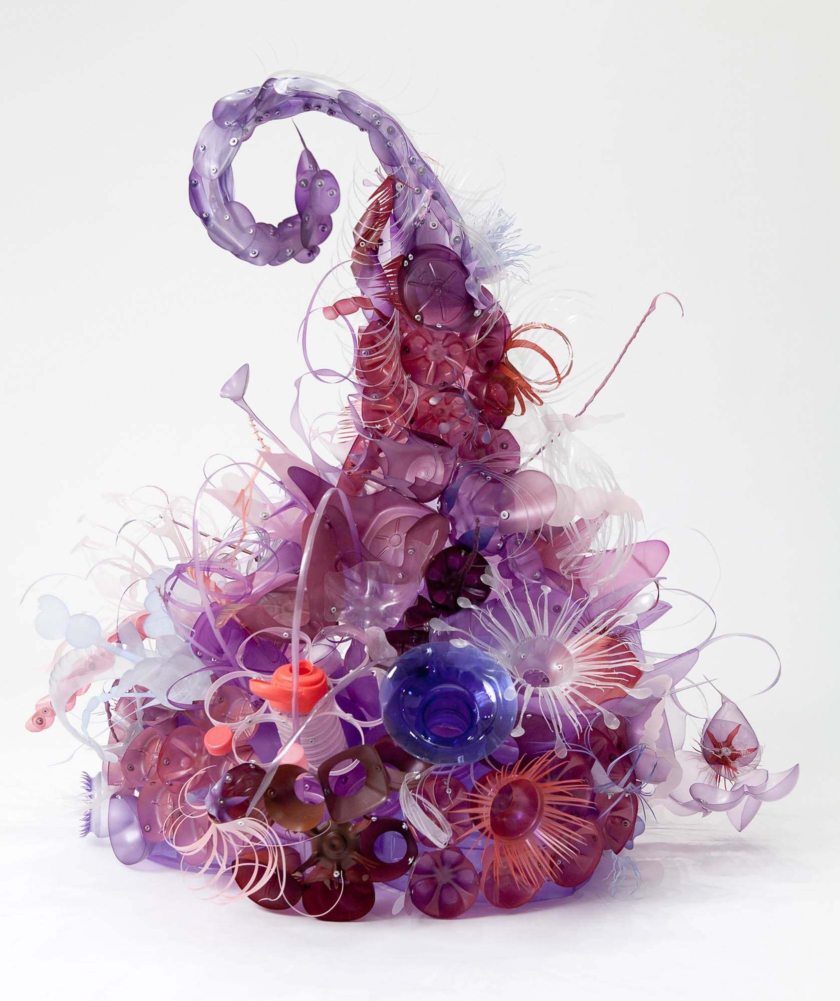 Sculpture created with red, white, and purple plastic detritus in the shape of a Hershey’s kiss. Individual pieces are shaped like sea anemones and coral polyps giving an overall impression of a coral reef.