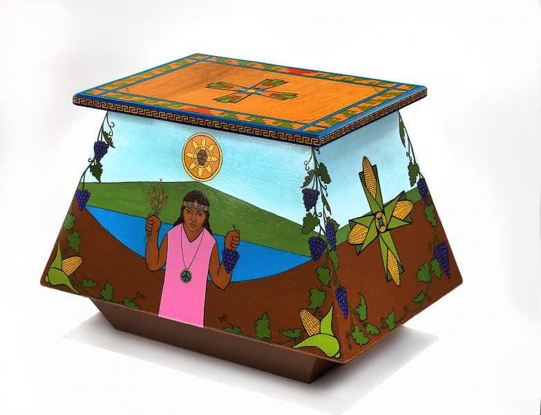 A vibrant painted box featuring a scene of a person in a pink shirt and headband holding grapes and herbs, set against a backdrop of hills, a river, and a bright sun. The box's sides are adorned with grapevines, cornstalks, and decorative patterns.
