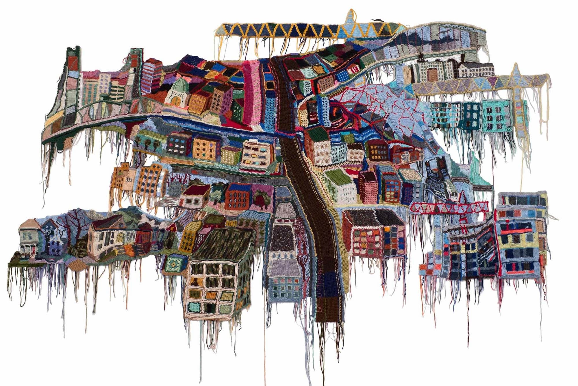  A detailed, colorful crochet artwork depicting an urban landscape with buildings, bridges, and a variety of architectural elements, all crafted from yarn.