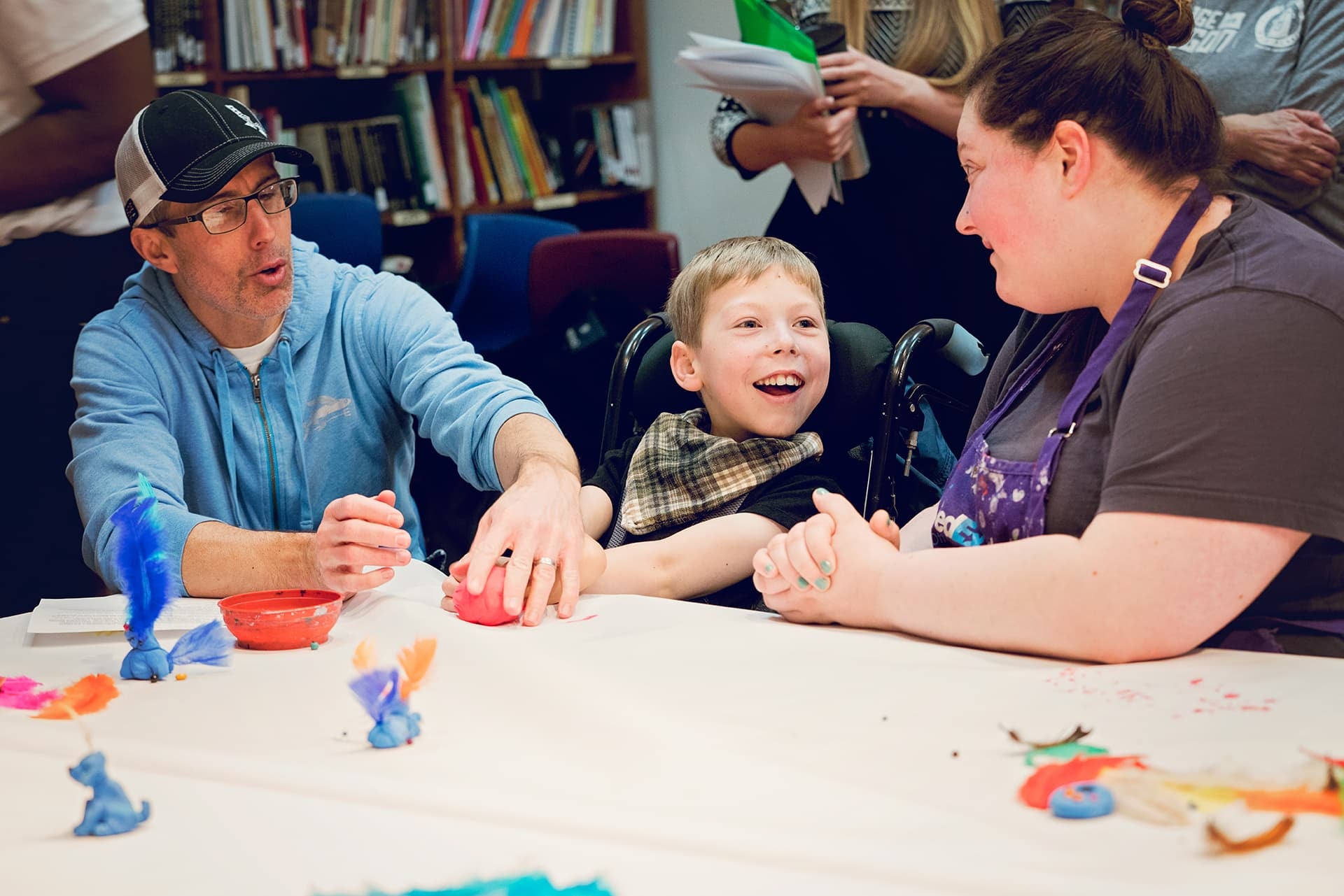 A child with their dad sit at a table in an art studio with an art teacher.