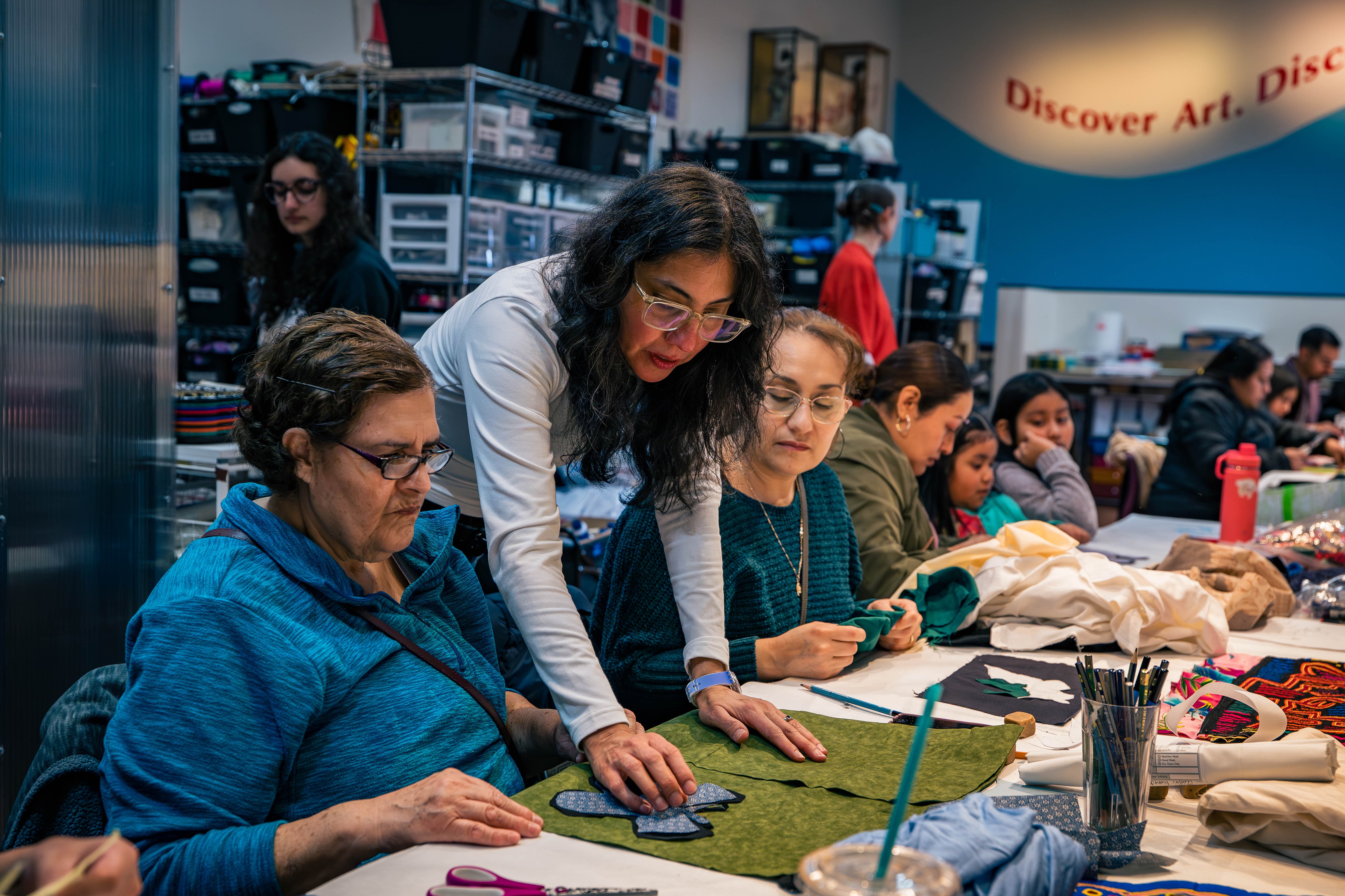 An art instructor helps two women at a table filled with art supplies