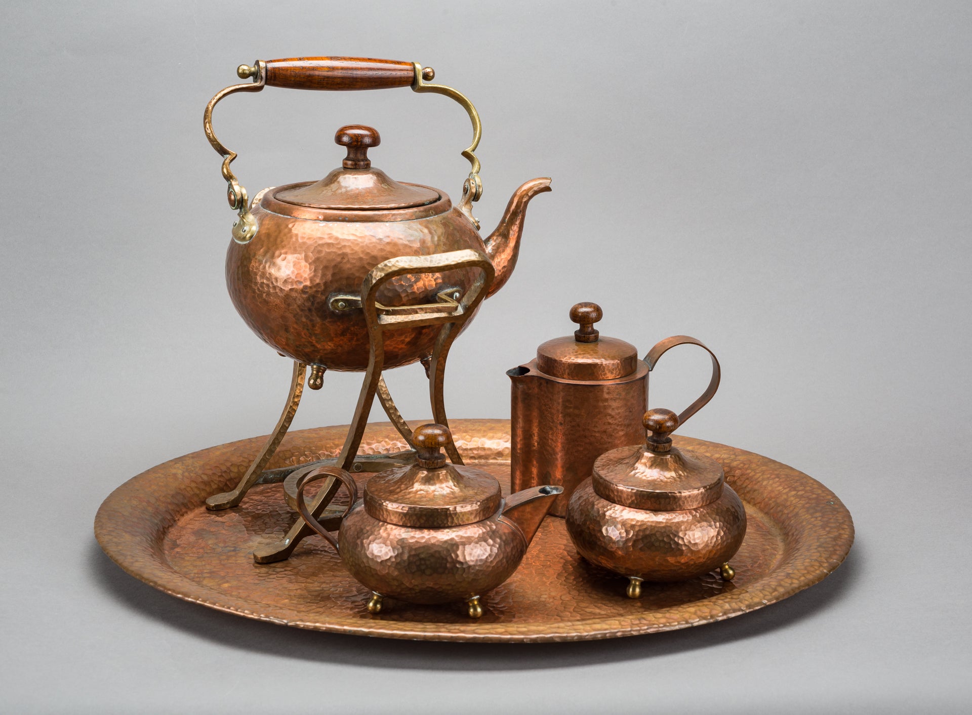 A brass serving platter with a tea service of brass on top. There is a large teapot with legs, a sugar bowl, a creamer and a honey pot.