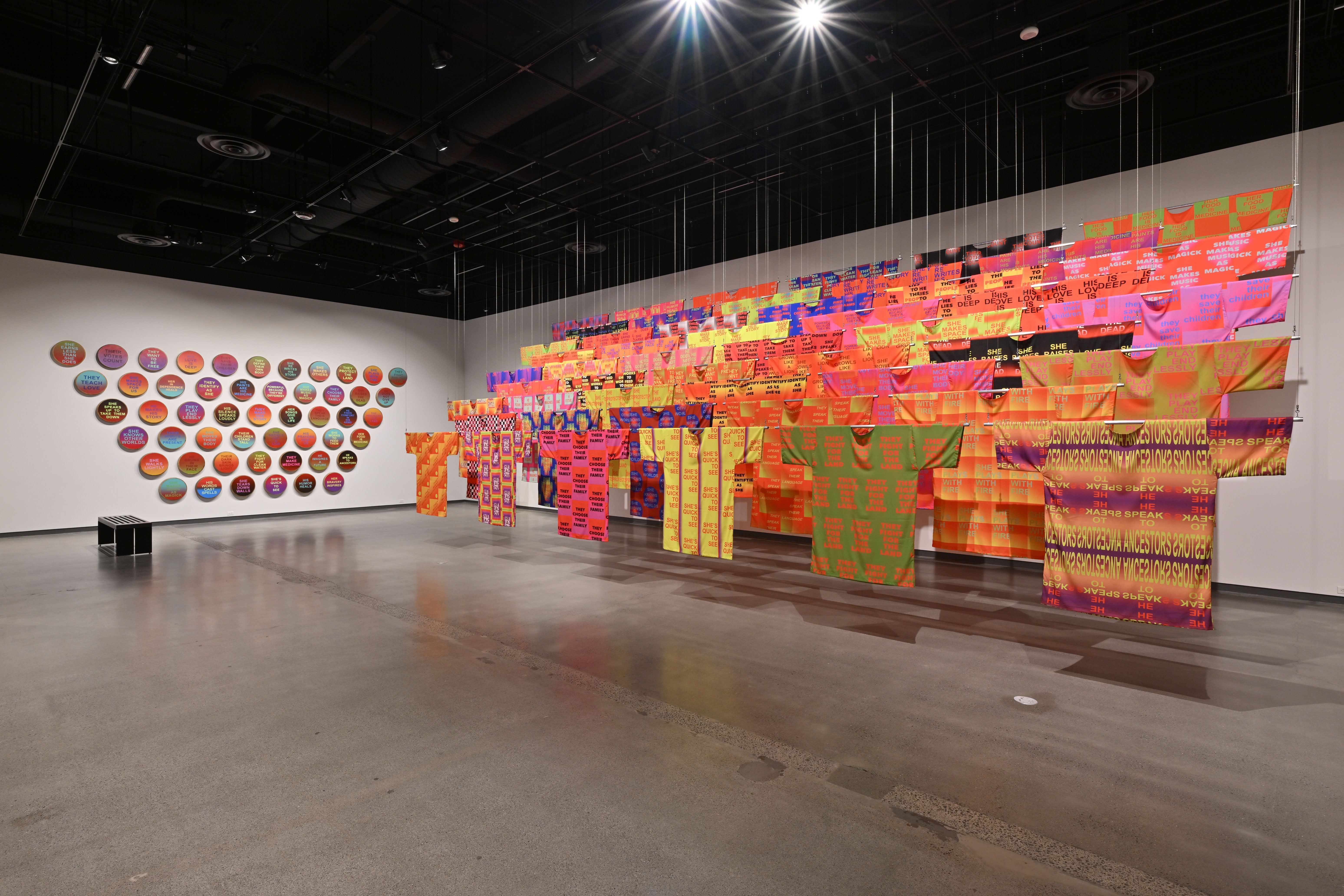 Gallery view of a multicolored installation of textiles including clothing and wall art.